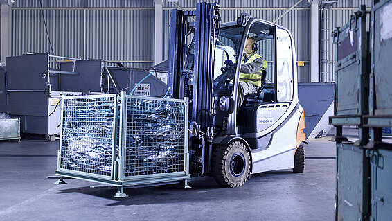 A Leadec employee driving with a forklift with a pallet of waste through factory. 