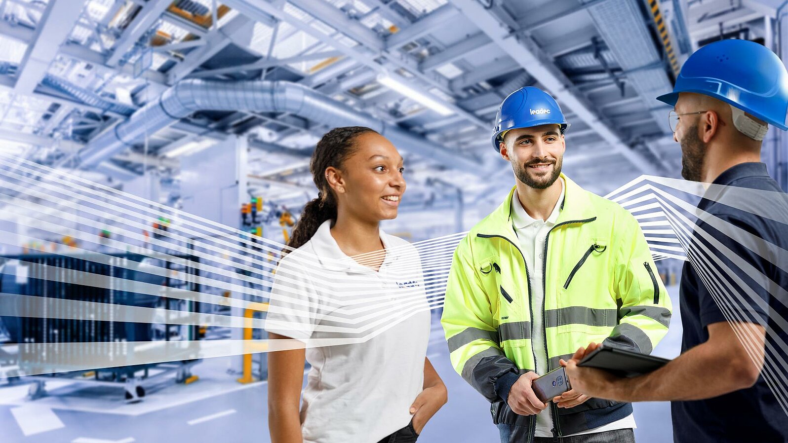 Three Leadec employees in workwear talking in front of a factory background.