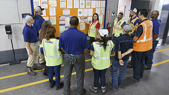 Leadec employees standing in front of a display board discussing tasks.