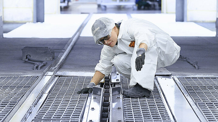 Leadec employee inspecting and cleaning floor grids in a paint shop.