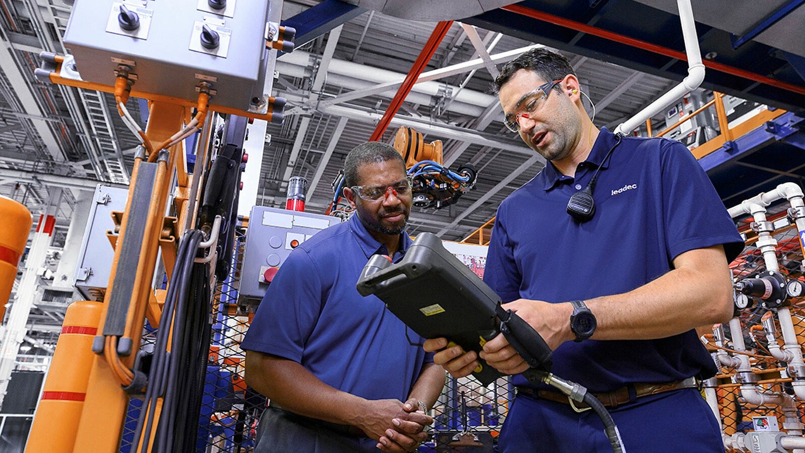 Two Leadec employees working with a controller at a robot to optimize processes.