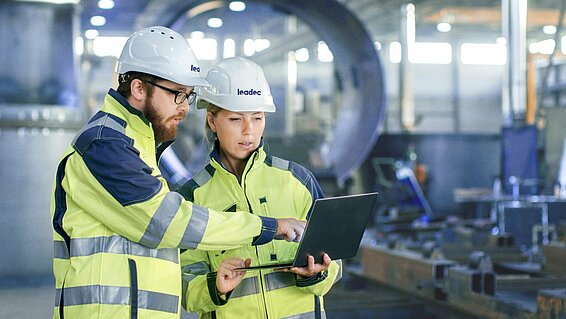 Man and woman inside a factory, both wearing safety clothing and helmets.