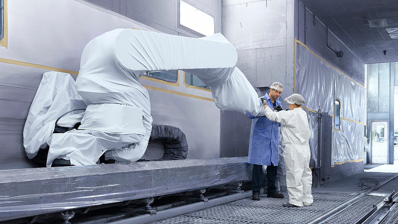 Two Leadec employees working on a covered robot inside a paintshop.