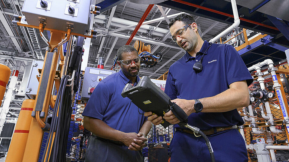 Two Leadec employees working with a controller at a robot to optimize processes.