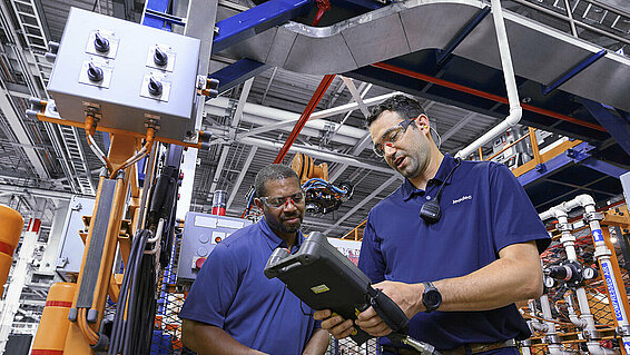 Two Leadec employees working with a controller at a robot to optimize processes.