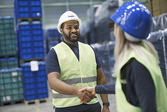 A male and a female Leadec with safety vests and helmets employee shaking hands in a warehouse.