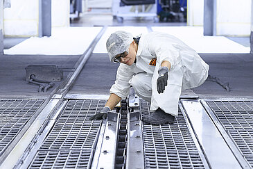 Leadec employee inspecting and cleaning floor grids in a paint shop.